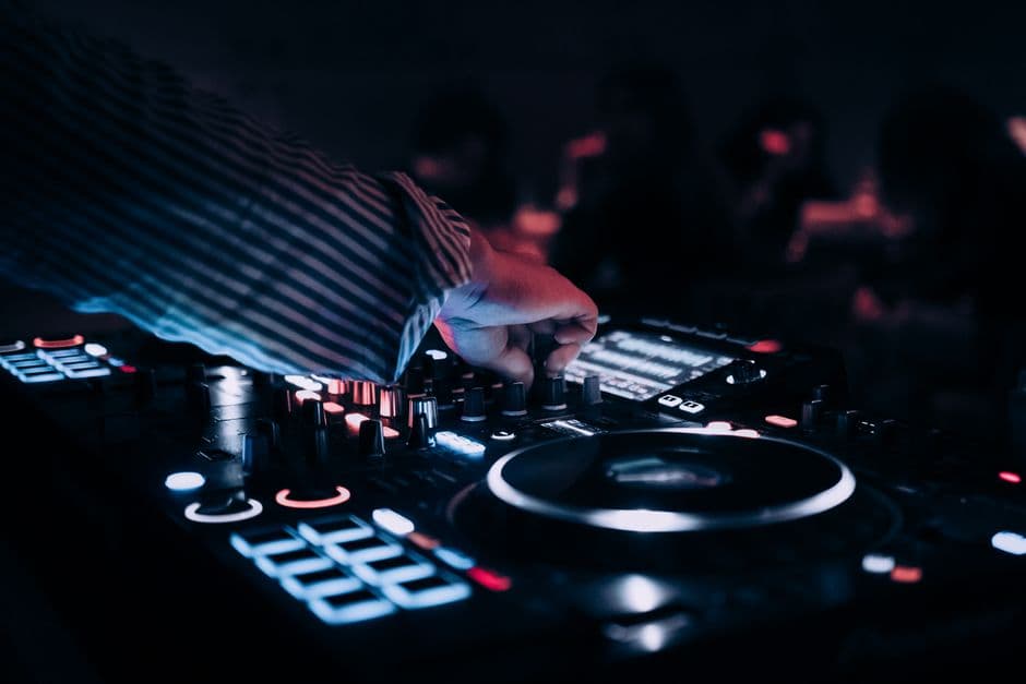 Hånd på en opplyst DJ-konsoll med glødende knapper i et mørkt lokale
