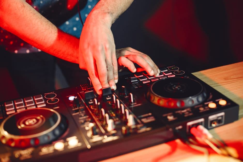 Hender som mikser på en DJ-controller i varmt rødt lys